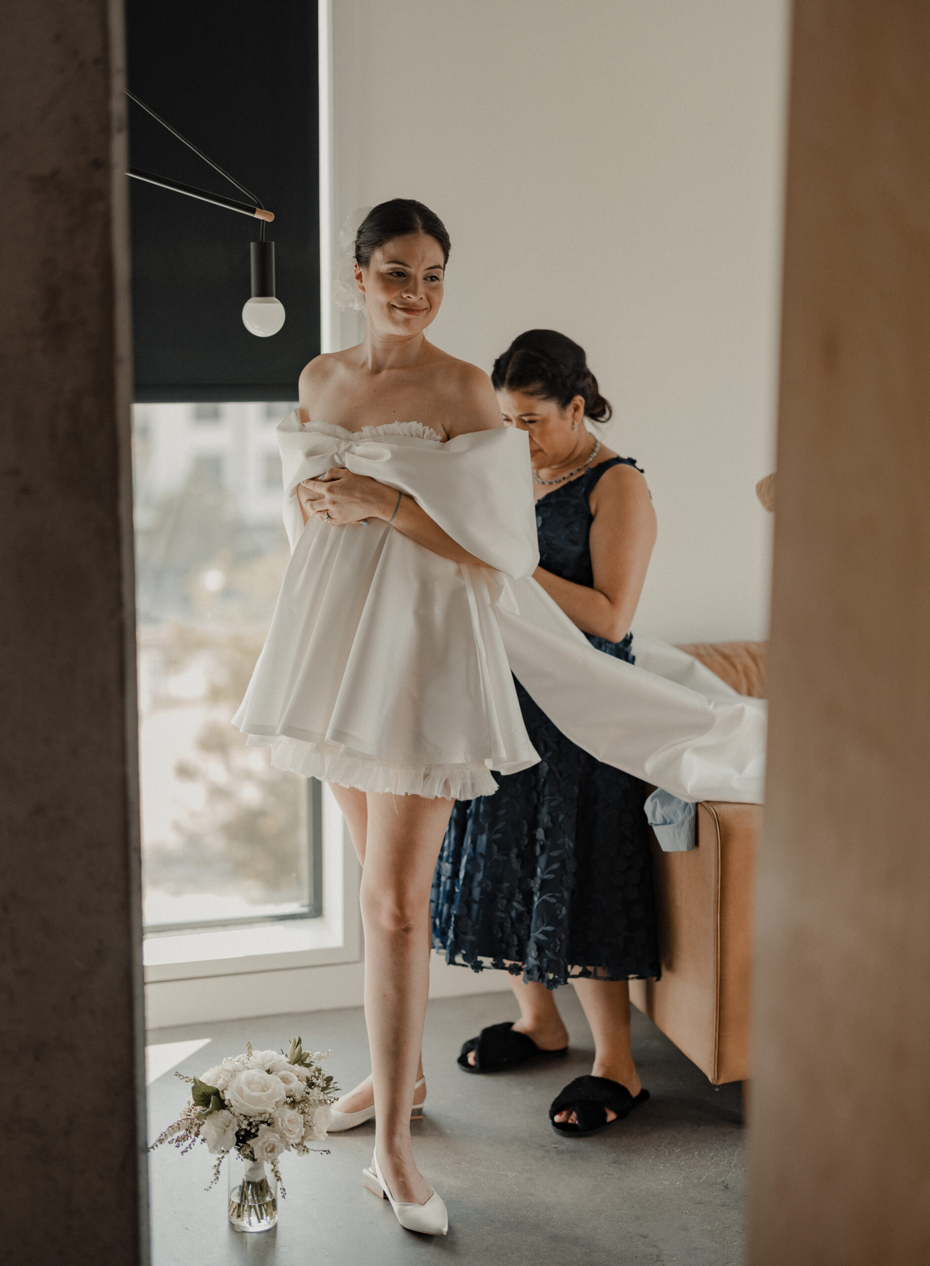 woman getting into her wedding dress on wedding day with her mother zipping up her zipper in the back, white wedding dress, wedding day, wedding photography